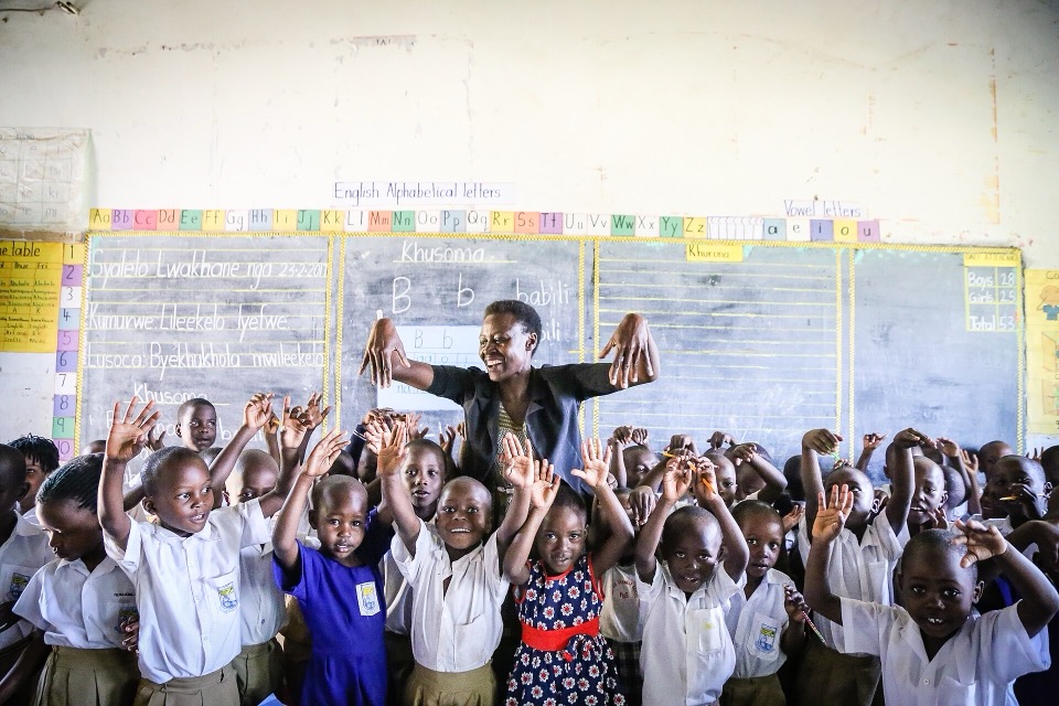 A classroom in Uganda with students and a teacher supported by USAID's School Health and Reading Program — rows of children at wooden desks, bright natural light